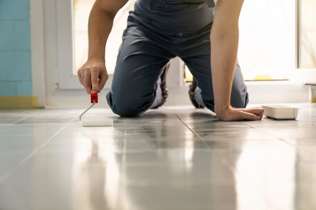 Unrecognizable house painter, kneeling while painting the floor tiles in the kitchen