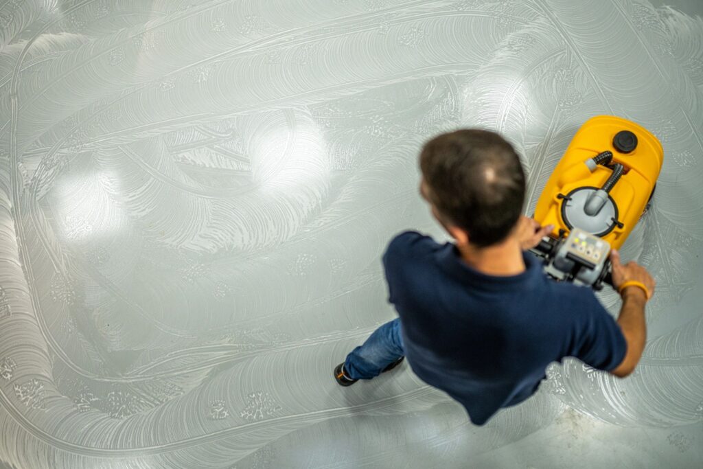 Male Worker Operating Yellow Floor Scrubber on Workshop Surface